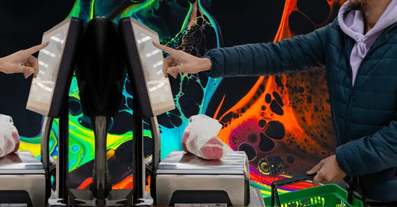 A mirrored image of a man in a purple hoodie and navy puffer coat holding a green grocery basket and touching the screen of a self-checkout kiosk.